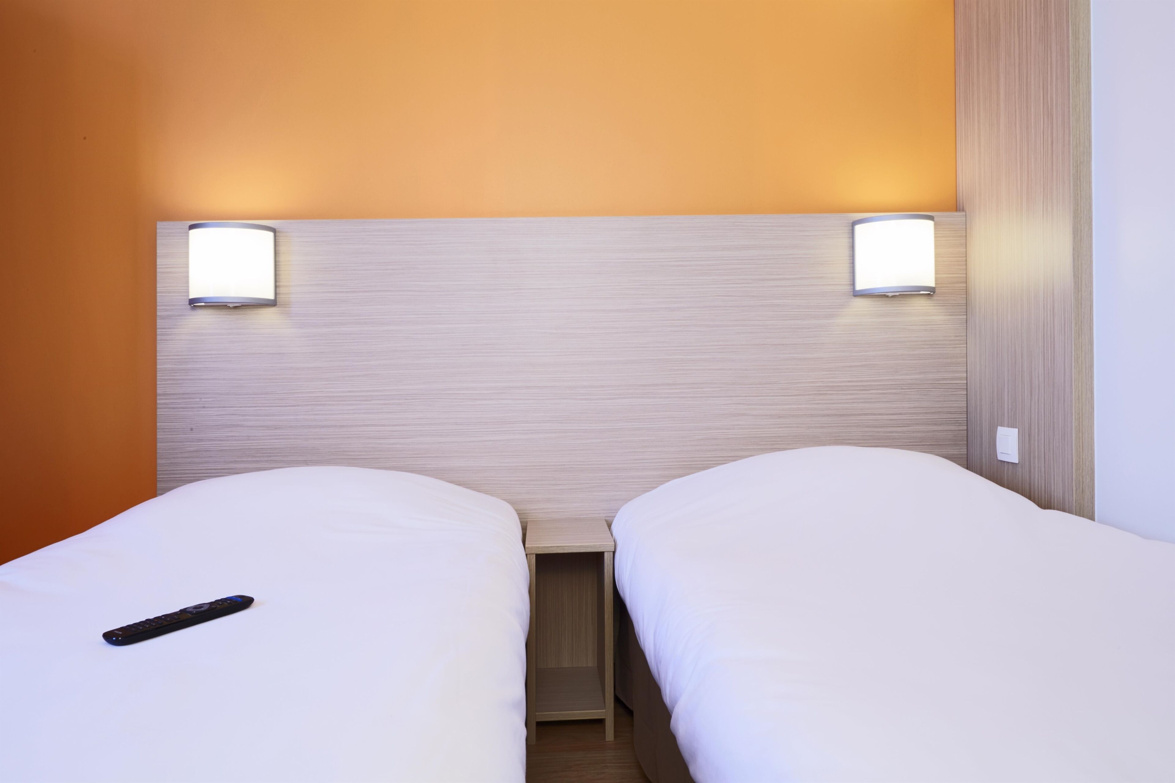 Een hotelkamer met twee eenpersoonsbedden, een nachtkastje ertussen en twee wandlampen.