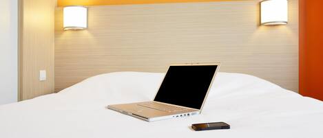 A hotel room with a bed, a laptop, and a smartphone on the bed.