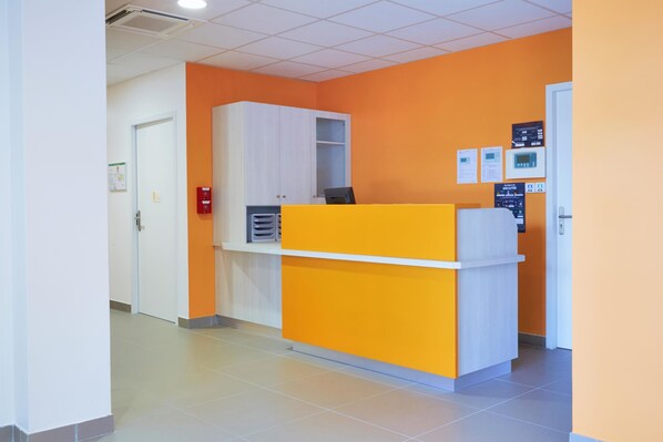 Un área de recepción con una pared de color naranja brillante, un mostrador de recepción blanco y una puerta blanca.