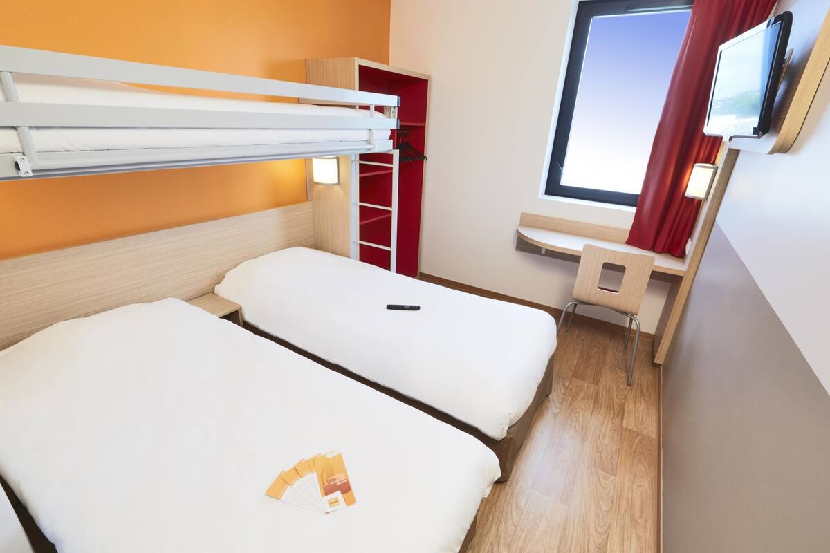 A hotel room with two beds, a desk, a TV, and a wardrobe.