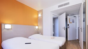A hotel room with two beds, a wooden headboard, a wall-mounted light, and a door leading to a bathroom. - Premiere Classe Bordeaux Ouest - Mérignac Aéroport (Merignac)