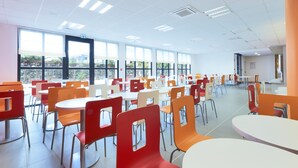 A cafeteria with multiple tables and chairs, large windows, and a bright interior. - Premiere Classe Bordeaux Ouest - Mérignac Aéroport (Merignac)