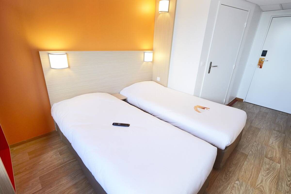 A hotel room with two single beds, a wooden floor, and a door with a handle.