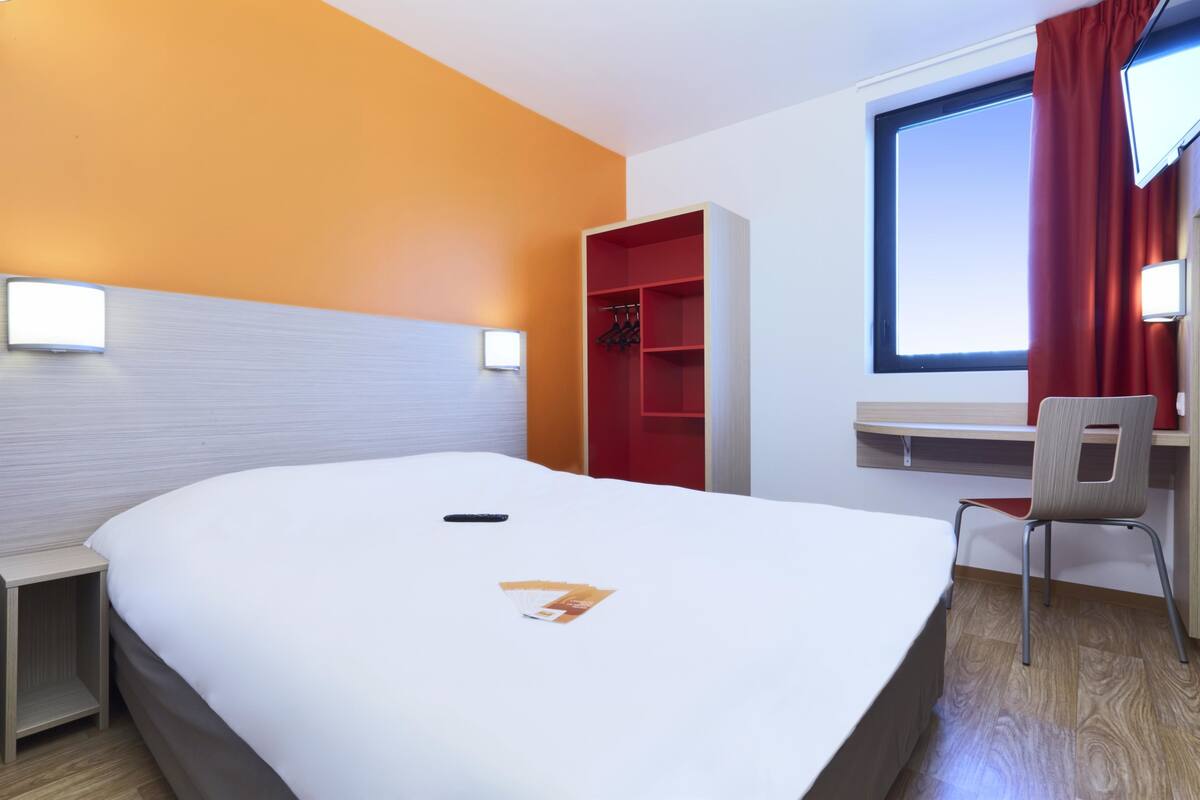 A hotel room with a large bed, a desk with a chair, a wardrobe, and a TV.