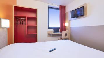 Una habitación de hotel con una cama, un escritorio con una computadora portátil, un televisor montado en la pared y un armario rojo.