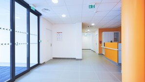 A clean, modern hallway with glass doors, a reception area, and a tiled floor. - Premiere Classe Bordeaux Ouest - Mérignac Aéroport (Merignac)