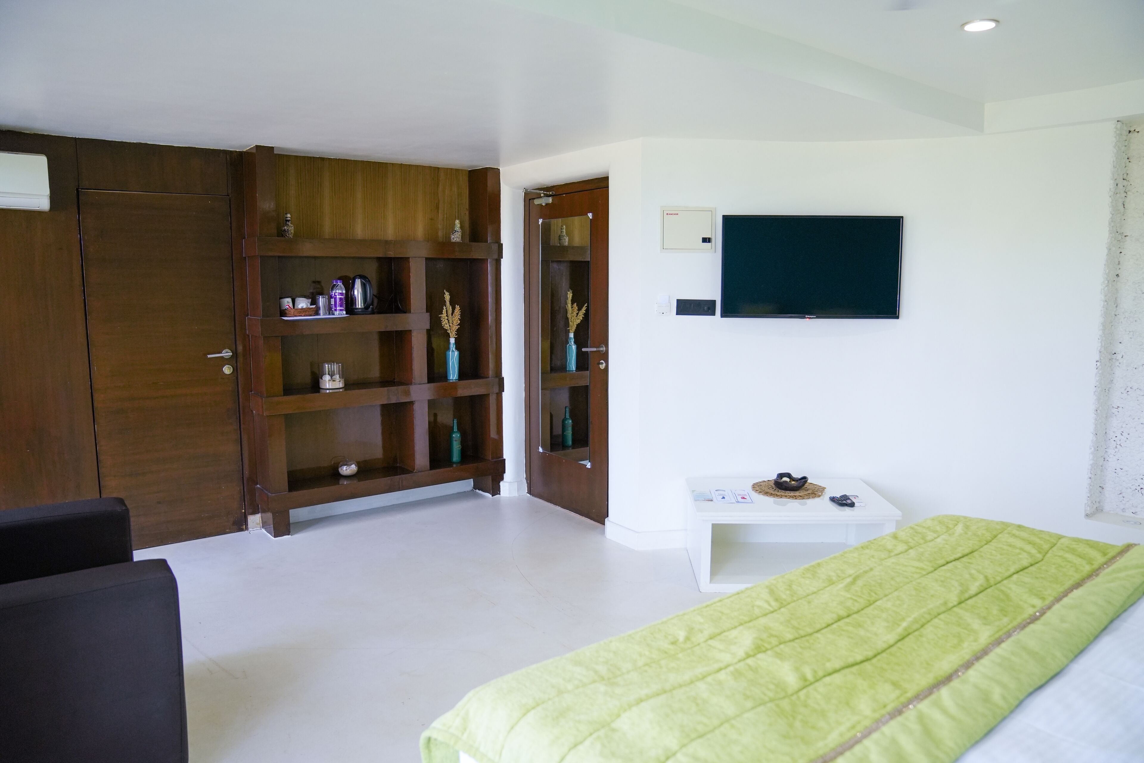 Quarto com cama, televisão, guarda-roupa de madeira e mesa de cabeceira branca.