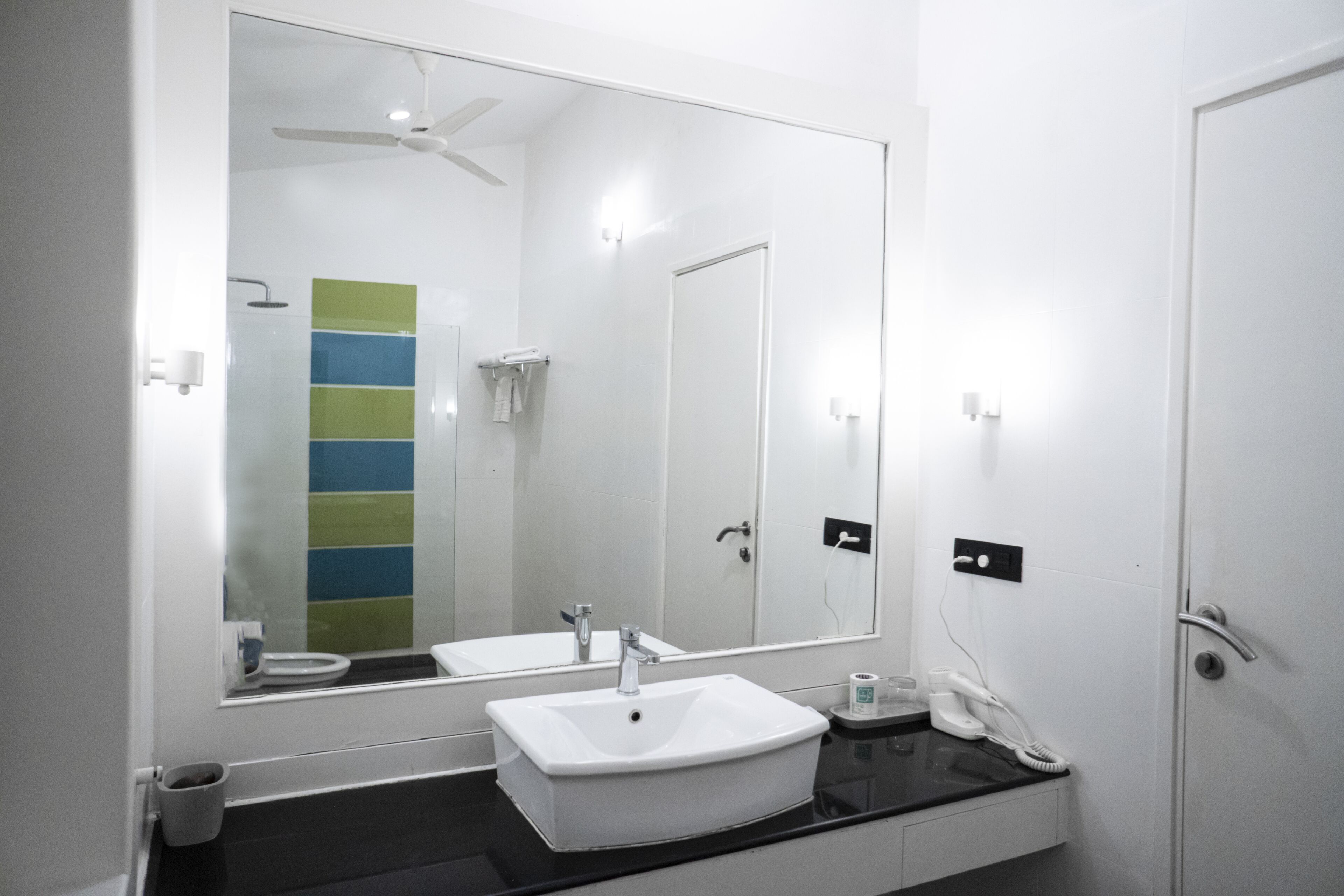 A modern bathroom with a large mirror, white sink, and a shower area.