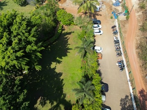 An aerial view of a parking lot with several cars and motorcycles, surrounded by lush greenery and palm trees.