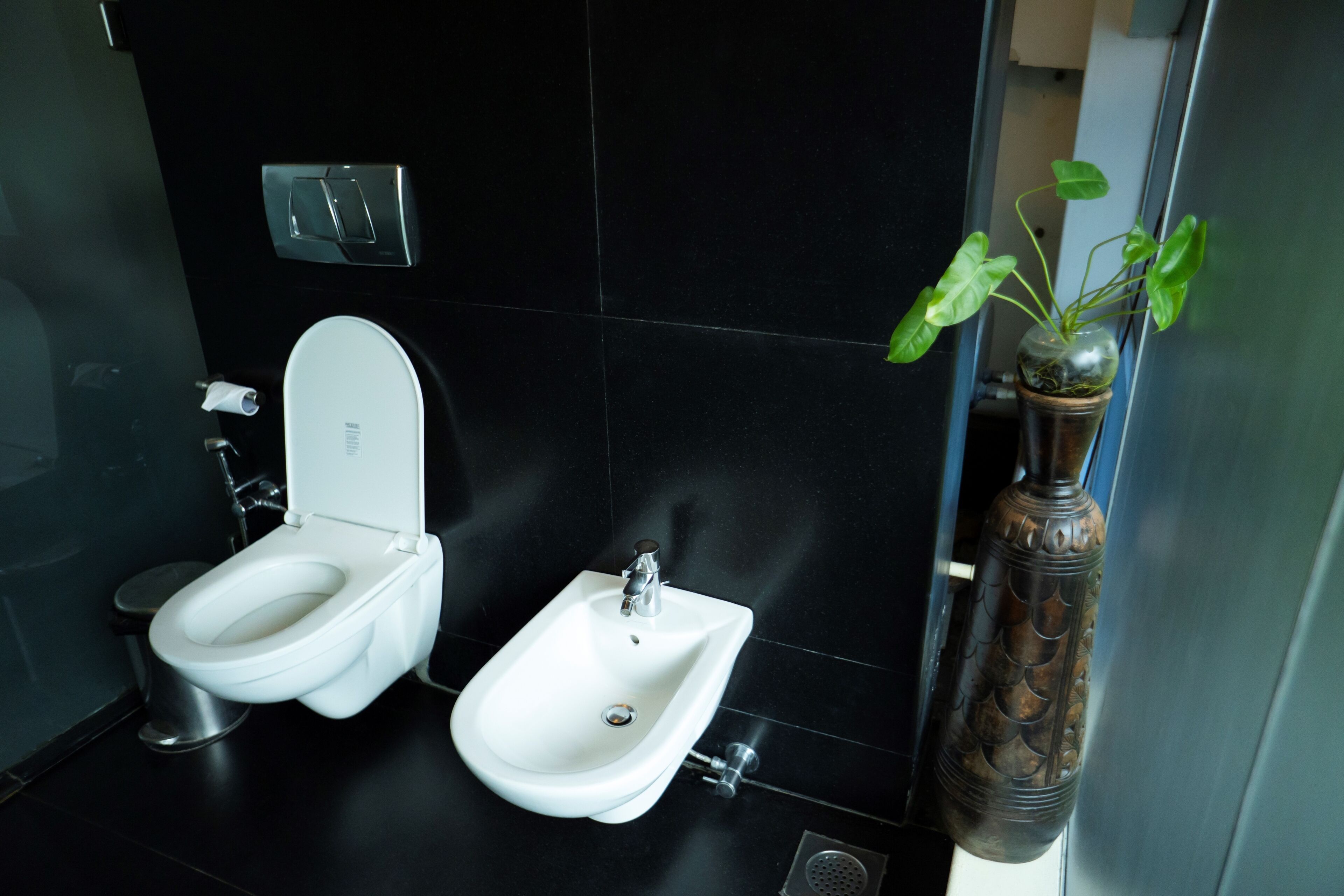 Un bany modern amb bidet, vàter i un ram de plantes verdes decoratiu.
