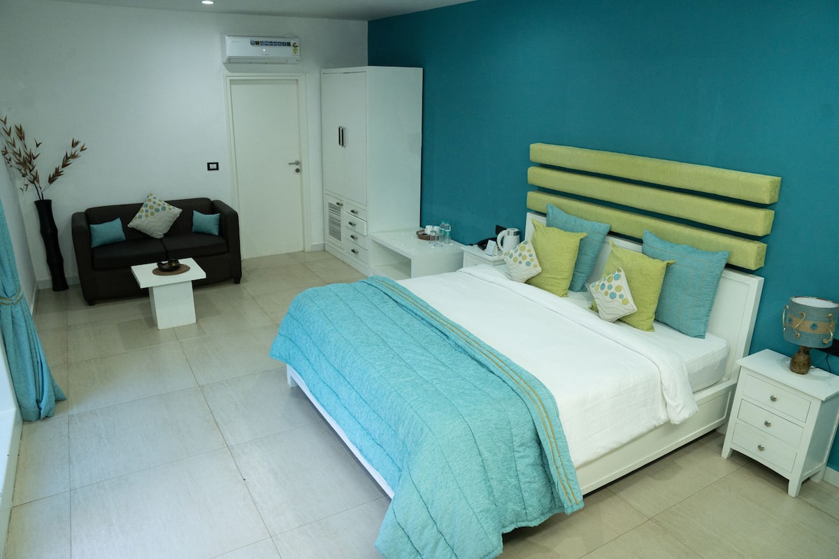 A bedroom with a bed, bedside table, nightstand, wardrobe, and a sofa.