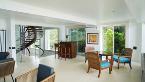 A spacious living area with a modern staircase, a dining table with chairs, and large windows offering a view of greenery. - Regenta Beach House Resort, Goa (Colva)