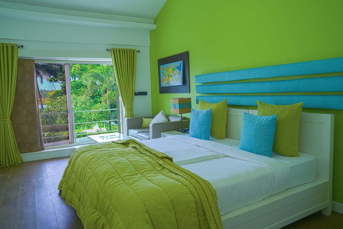 A bedroom with a large bed, a view of greenery outside, and a bright green wall.