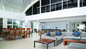 A spacious living area with a high ceiling, a grey sofa with blue cushions, wooden chairs, and a coffee table. - Regenta Beach House Resort, Goa (Colva)