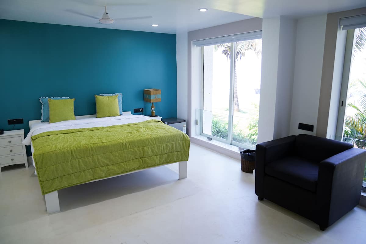 A bedroom with a bed, a chair, a nightstand, and a window with a view of palm trees.