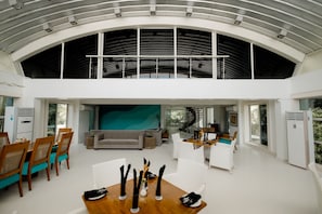A spacious living area with a high ceiling, a dining table set for four, and a modern staircase leading to an upper level.