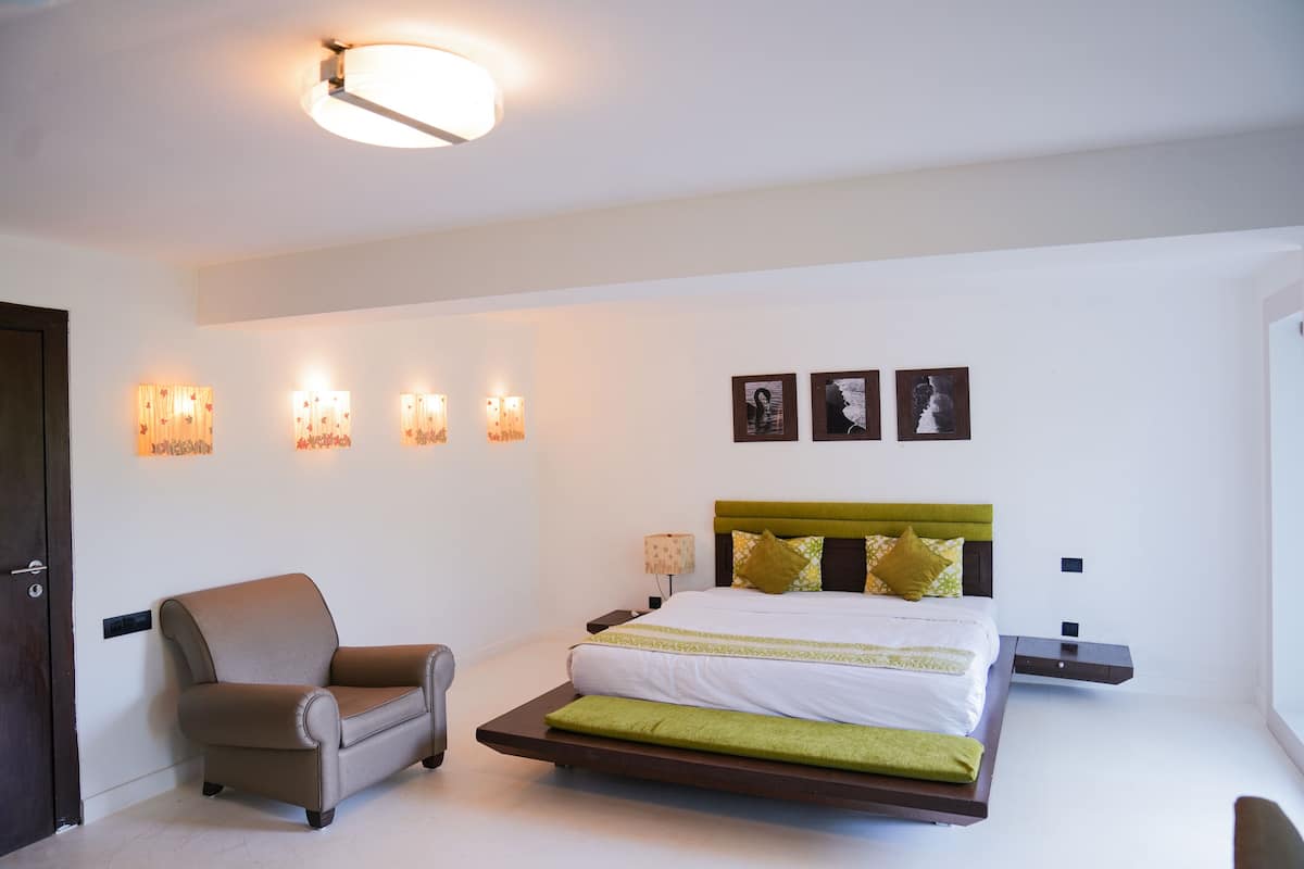 A modern bedroom with a bed, bedside tables, a chair, wall-mounted lights, and framed pictures.