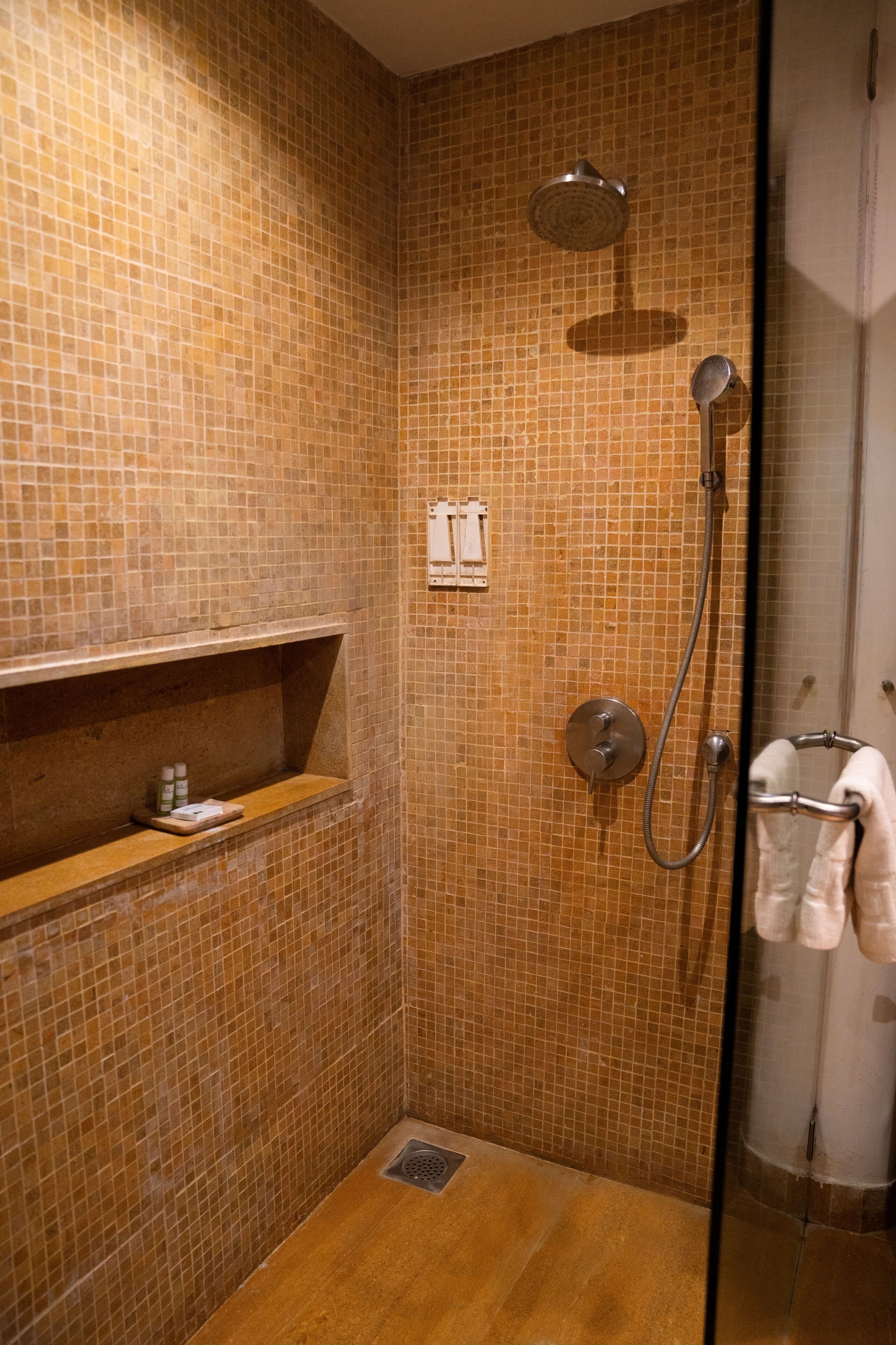 Een kleine betegelde badkamer met een glazen deur, een plank met toiletartikelen en een handdoekhouder.