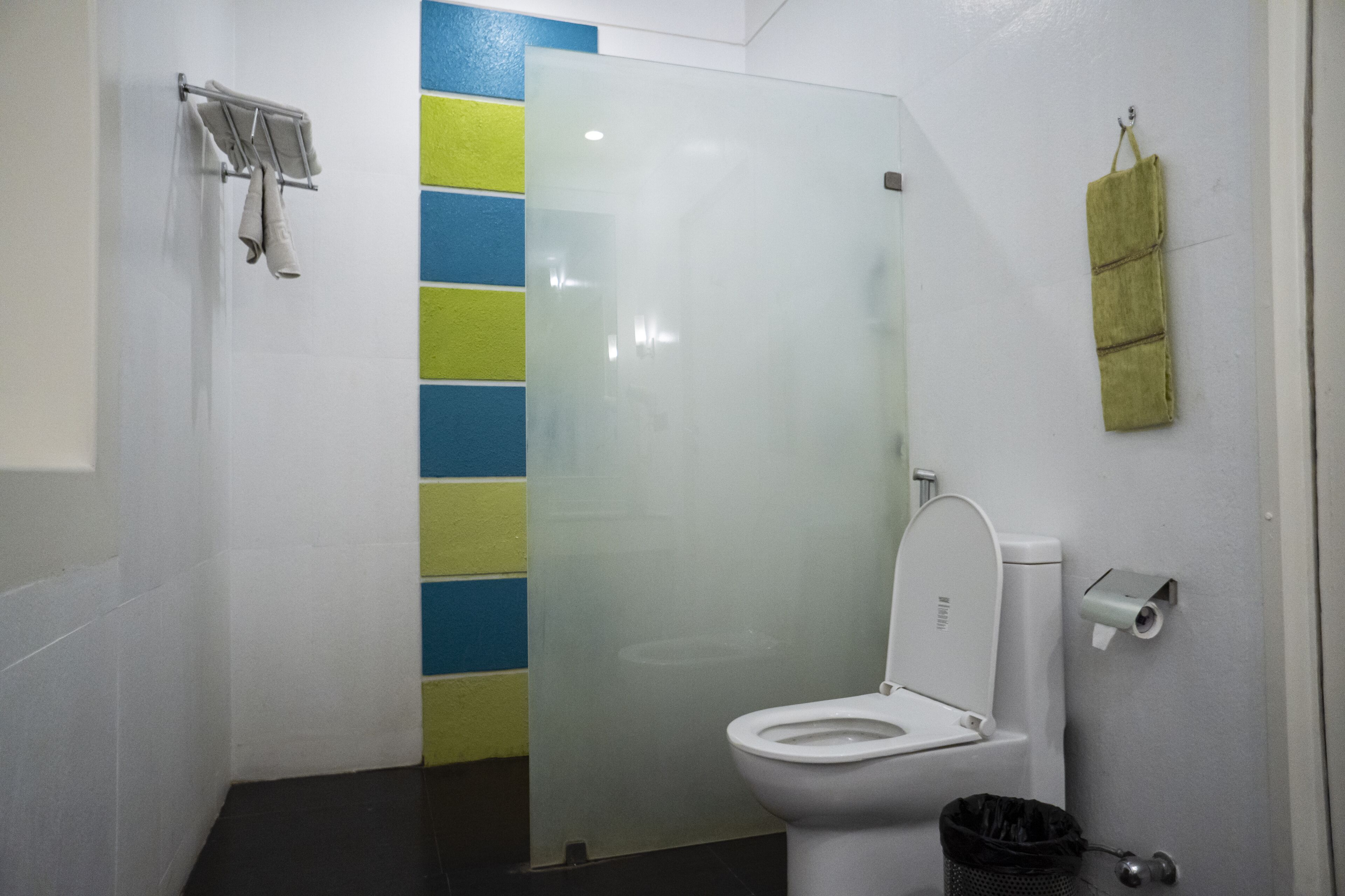 Un baño con inodoro, mampara de vidrio, toallero y un cubo de basura.