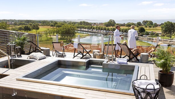 Un área de piscina en la azotea con dos jacuzzis, sillones de descanso y vistas del paisaje circundante.
