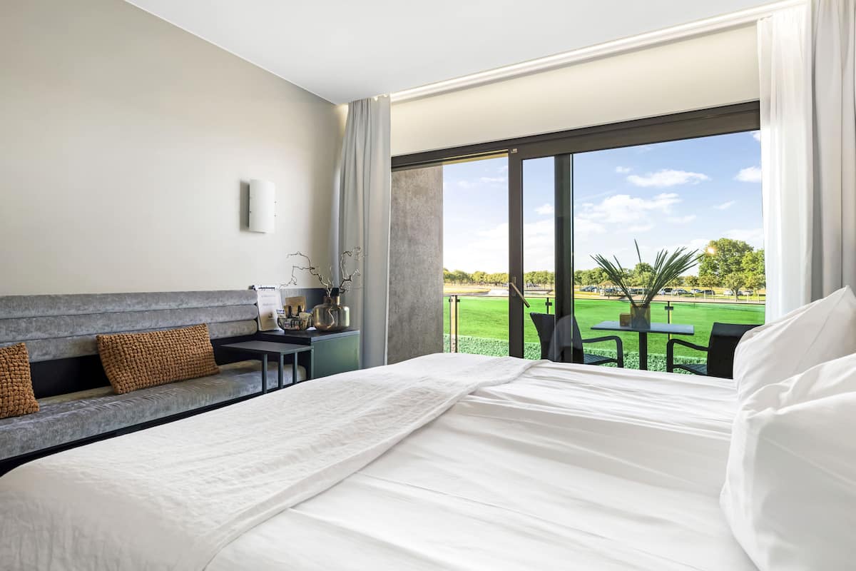 A hotel room with a large bed, a sofa, a small table with a vase, and a view of a golf course.
