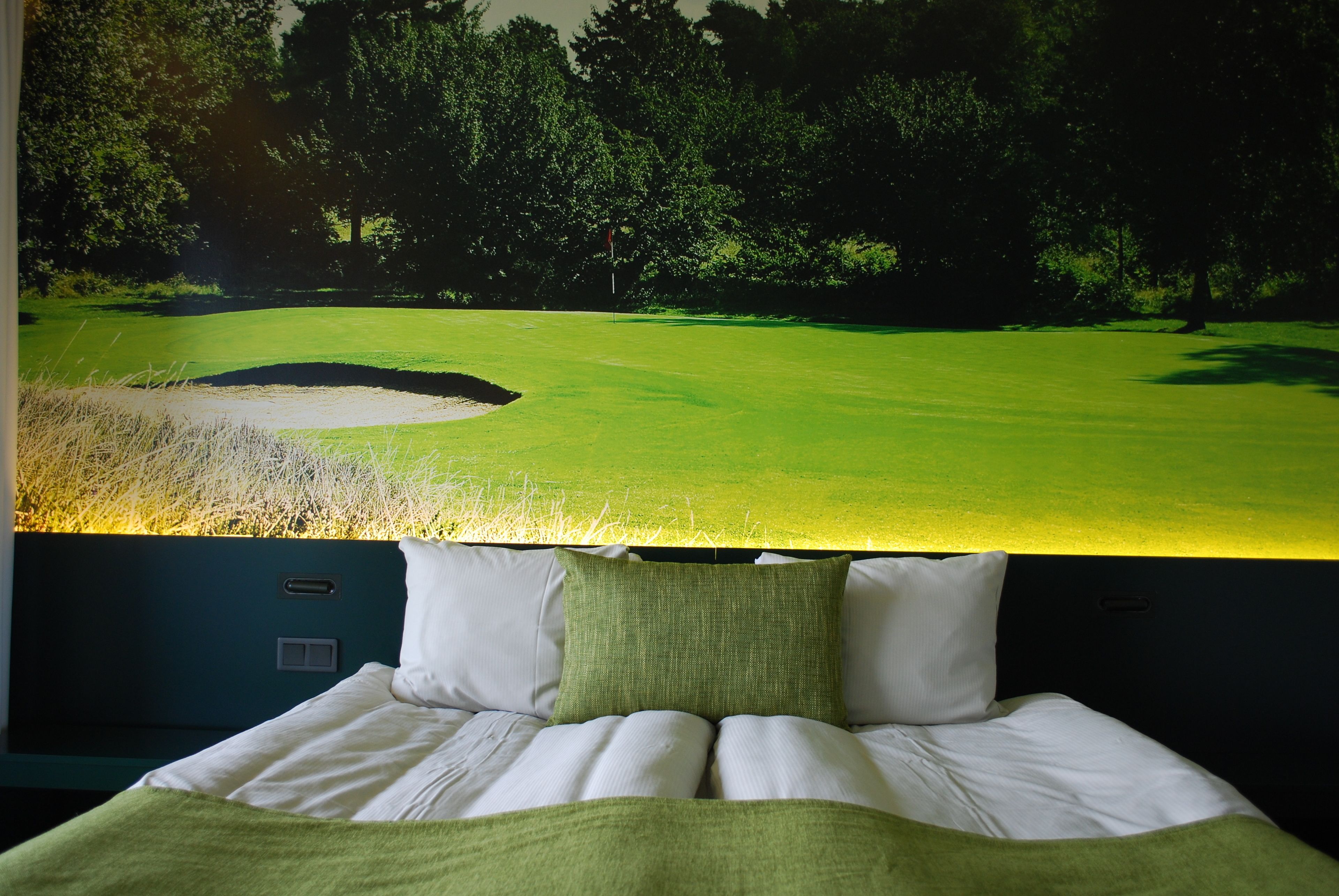 A bedroom with a bed, pillows, and a wall-mounted TV displaying a golf course.