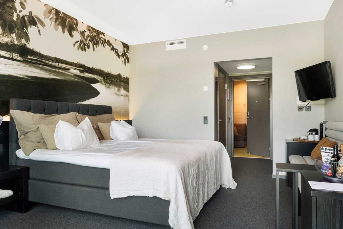 A hotel room with a large bed, a flat-screen TV, a desk with a computer, and a painting on the wall.
