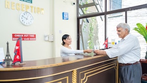 A reception desk with a clock, a sign indicating check-out time, and a flag. - Butterfly Lodge (Pokhara)