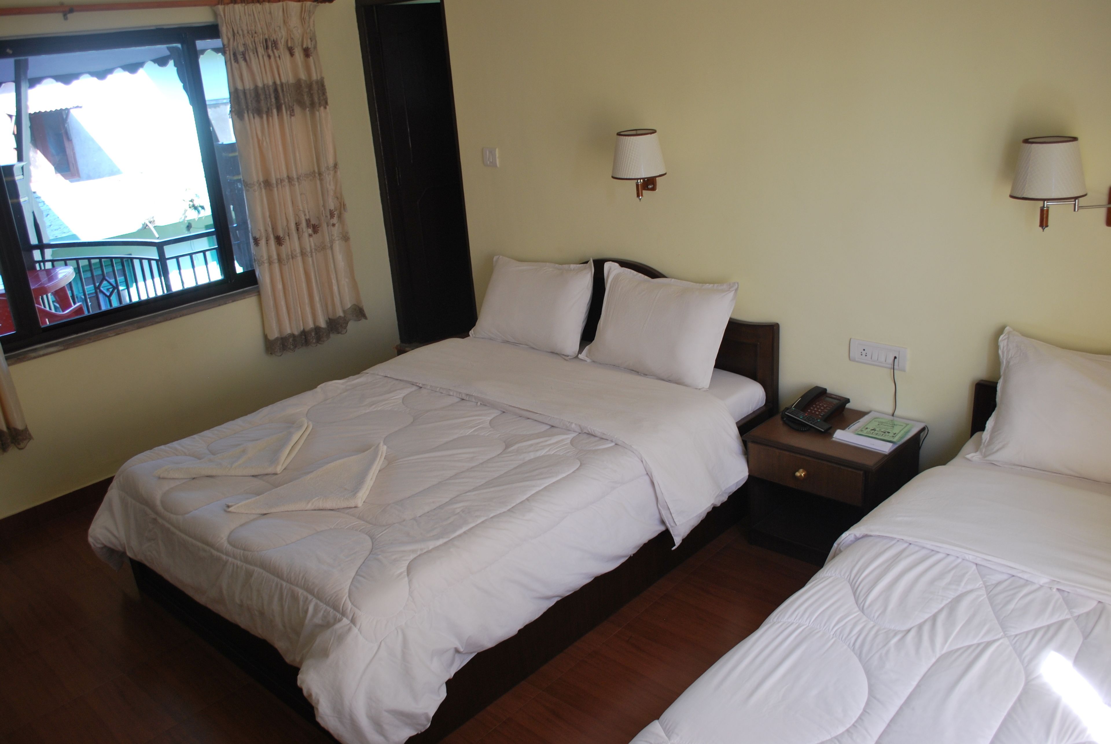 A hotel room with two beds, a nightstand with a phone and a lamp, and a window with curtains.