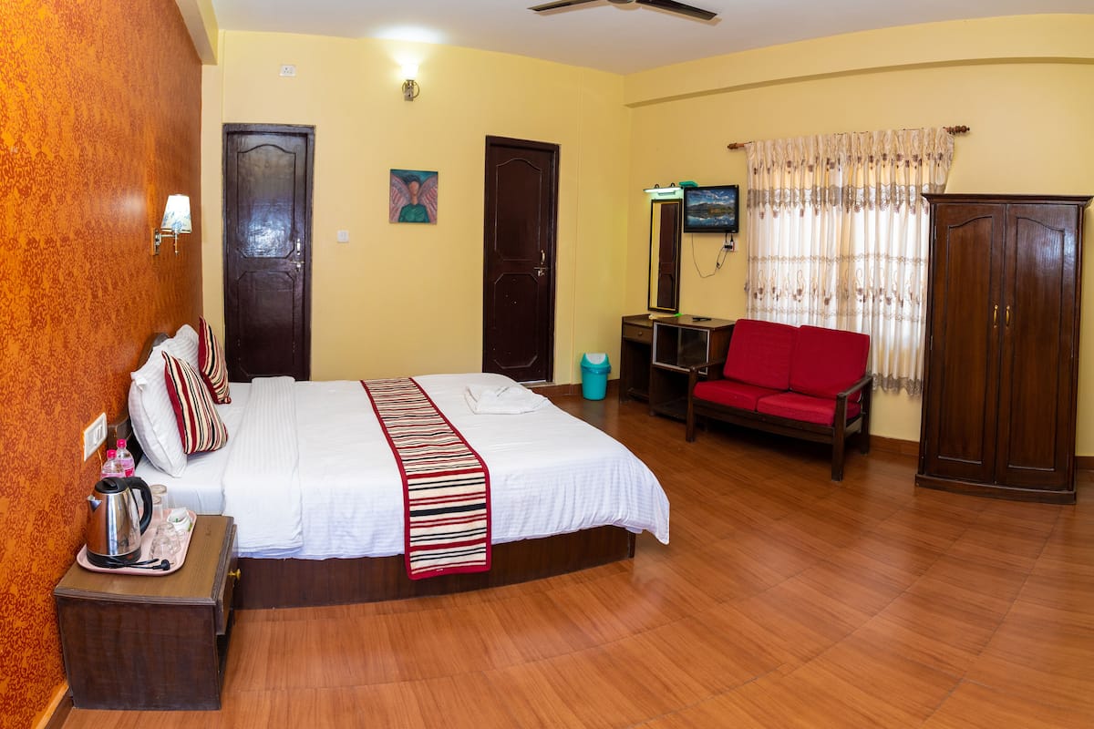 A hotel room with a bed, a red sofa, a wardrobe, and a ceiling fan.