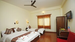 A hotel room with two beds, a red sofa, a wooden cabinet, and a ceiling fan. - Butterfly Lodge (Pokhara)