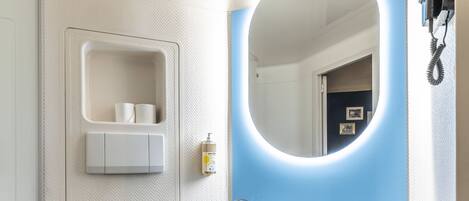 Un baño moderno con inodoro blanco, lavabo con espejo y zona de ducha.