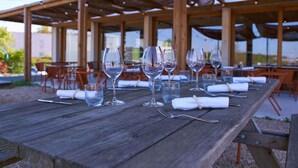 An outdoor dining area with wooden tables and chairs, clear glassware, and a thatched roof structure. - greet hotel Limoges Nord (Limoges)