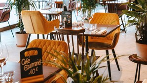 A restaurant interior with yellow chairs, tables, potted plants, and a menu sign indicating a price of 10€. - greet hotel Limoges Nord (Limoges)