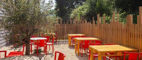 Un espacio al aire libre con mesas y sillas, rodeado por una valla de madera y árboles.