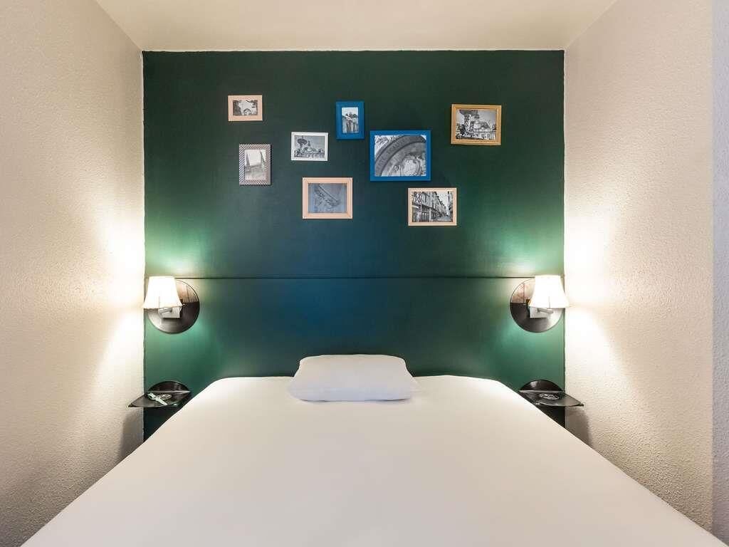 Una habitación de hotel con una cama, marcos de cuadros en la pared y lámparas de noche.