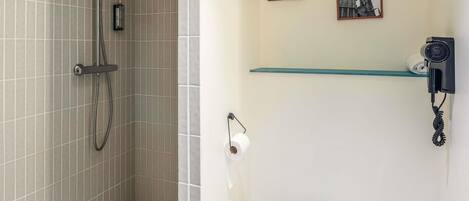 A bathroom with a shower, toilet, and a glass shelf with pictures.