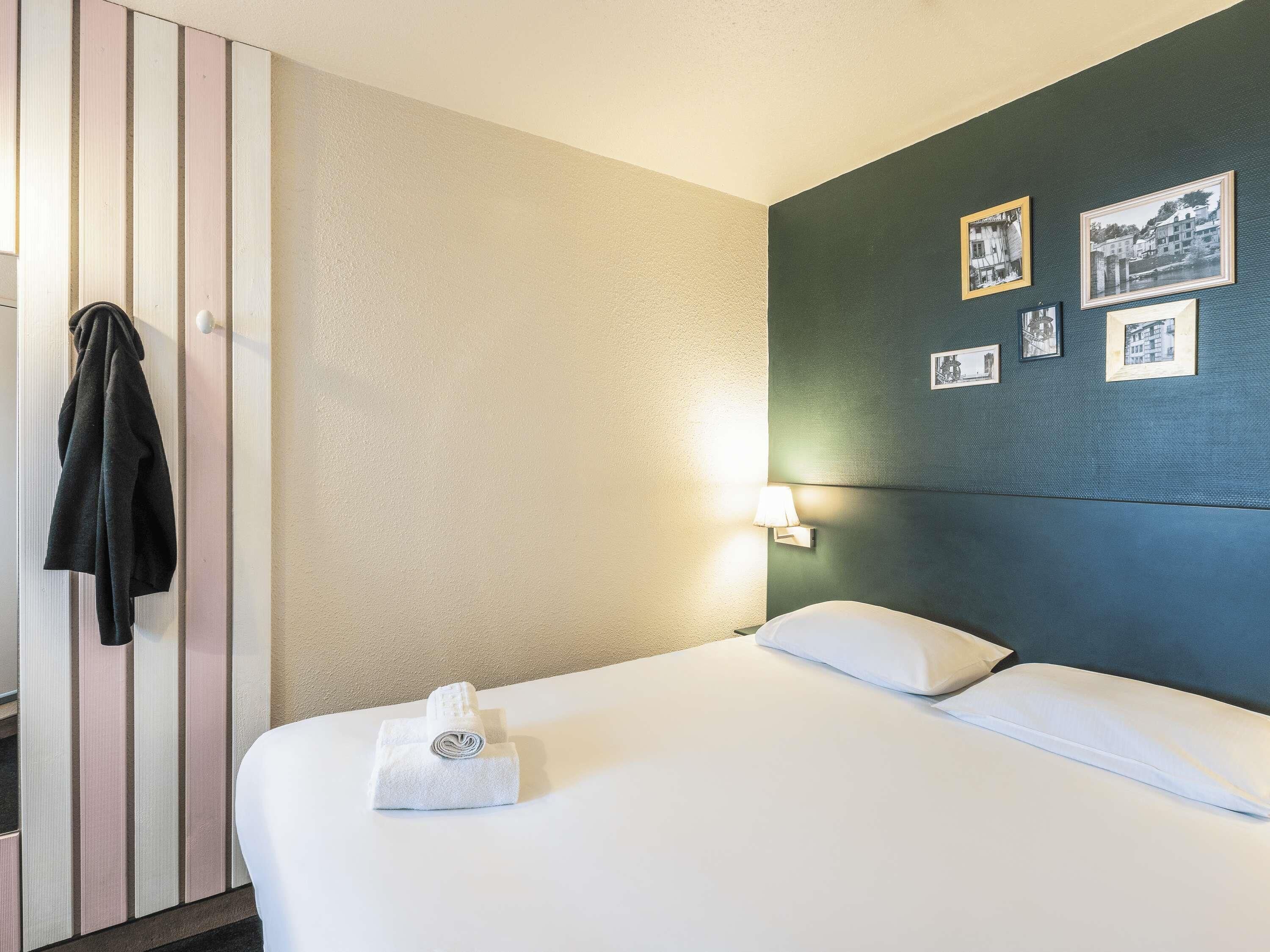 Habitación de hotel con cama, toalla, lámpara de pared y cuadros enmarcados.