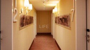Un couloir d’hôtel avec un plancher en bois, des portes numérotées et des luminaires fixés au mur.