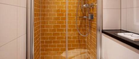 A modern bathroom with a glass-enclosed shower, white tiles, and a wooden floor.