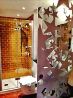 Bagno con cabina doccia in vetro, parete in mattoni a vista e pannello decorativo a motivi stellati.