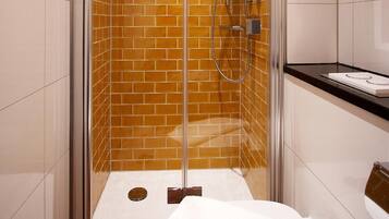 A glass-enclosed shower with a tiled wall, a white toilet, and a black countertop with a sink.