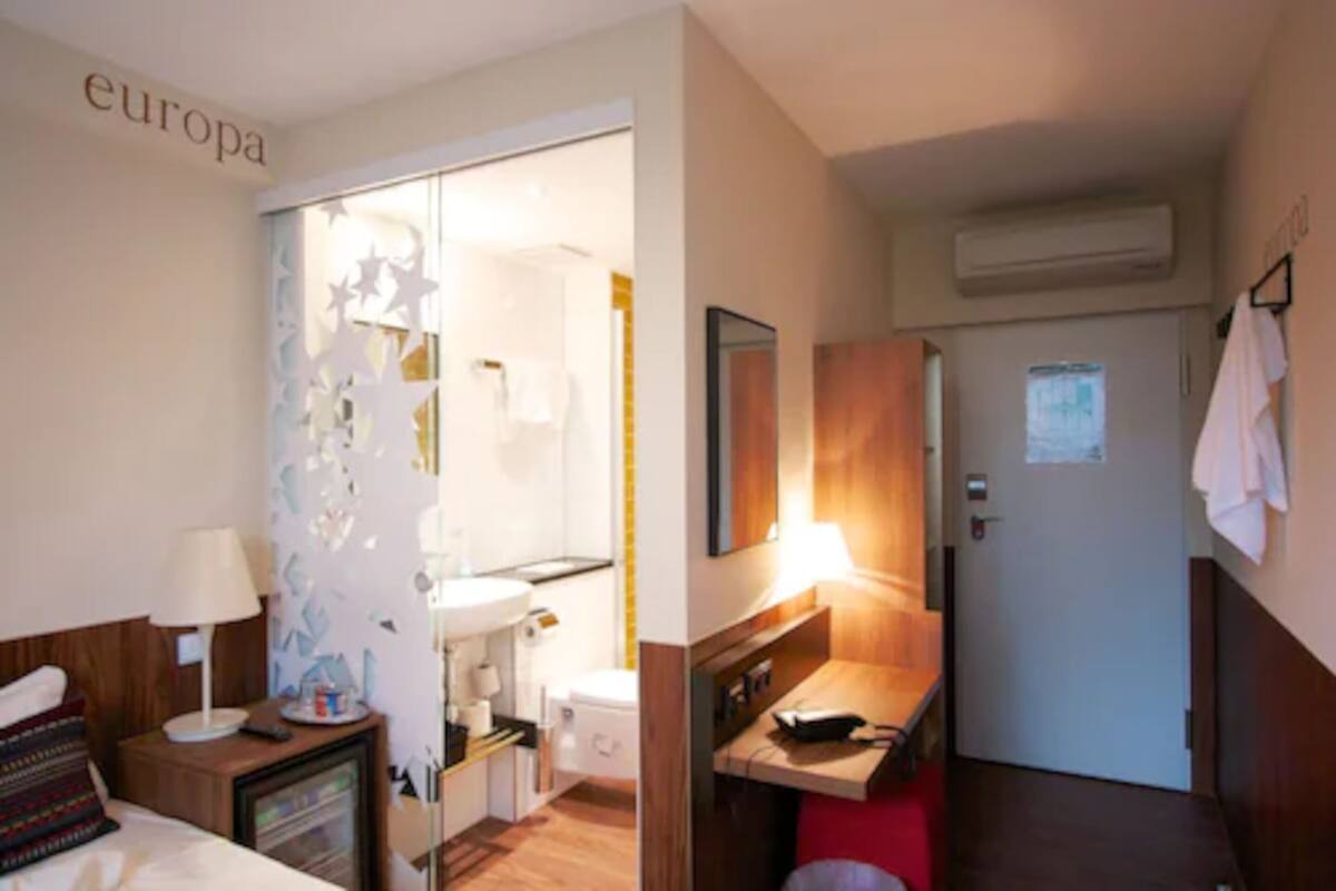 Hotellihuone, jossa on sänky, työpöytä, peili, pesuallas ja ovi, joka johtaa kylpyhuoneeseen.