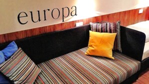 Un canapé avec un coussin à rayures et un oreiller, un mur sur lequel est écrit le mot « europa », et un panneau en bois derrière le canapé.