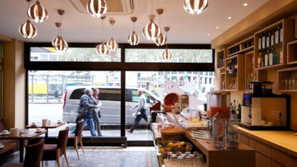 L’intérieur d’un café, avec des lampes suspendues, un comptoir où sont servis des boissons, et une vue sur la rue.