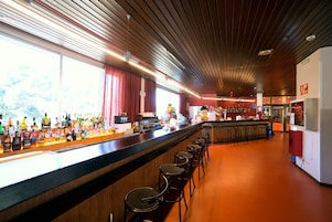 Zona de bar con una barra larga, varios taburetes y una amplia variedad de botellas.