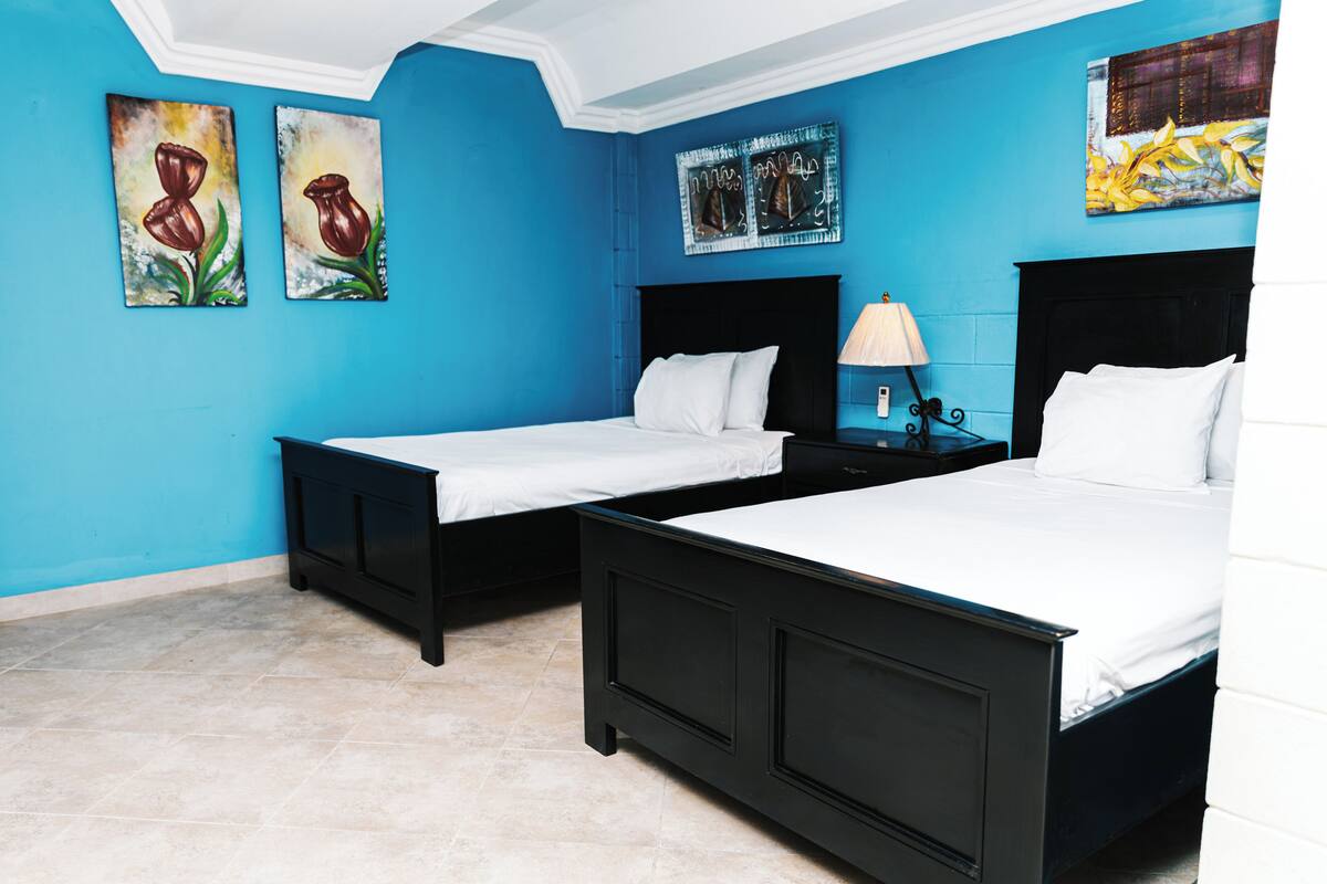 A hotel room with two beds, a nightstand with a lamp, and artwork on the walls.