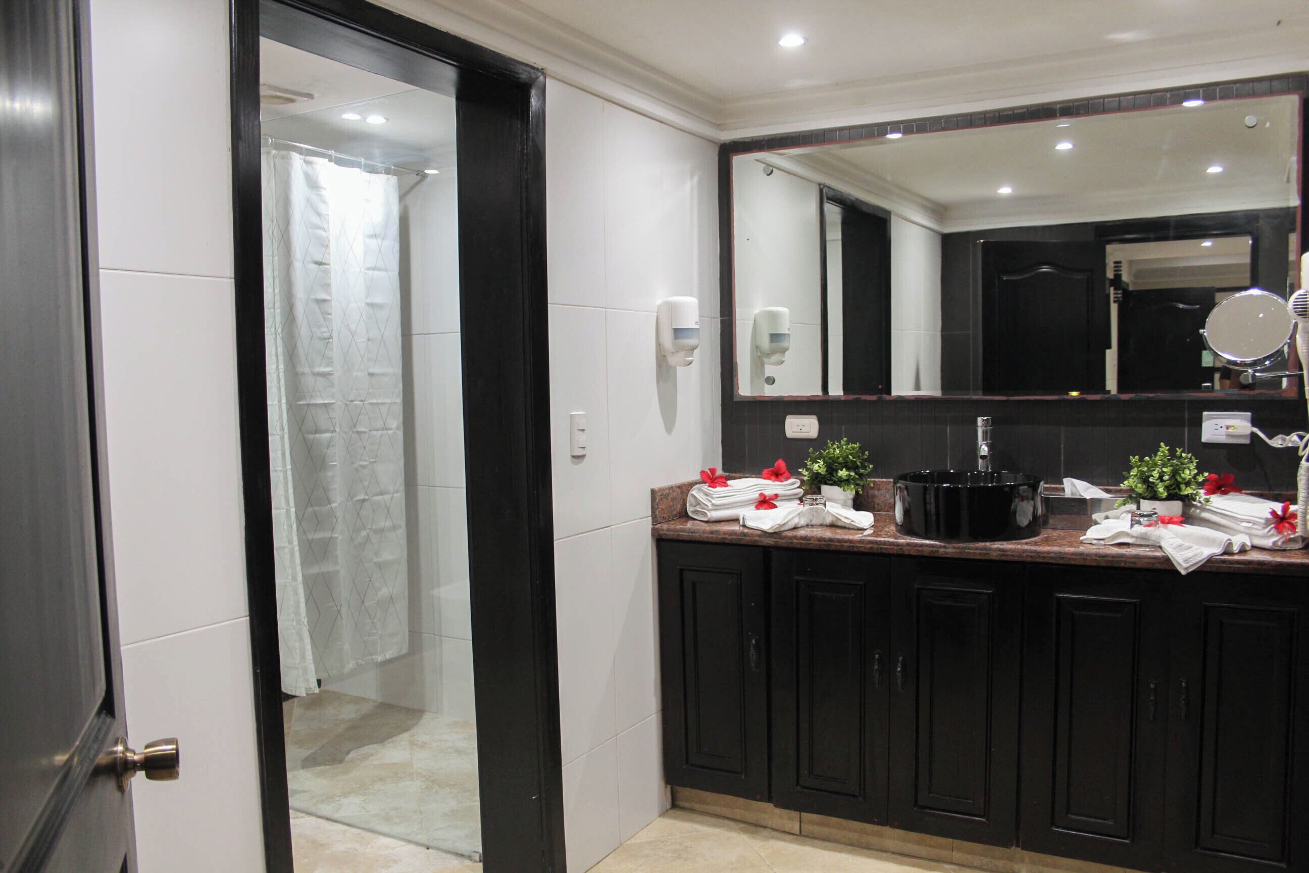 A modern bathroom with a large mirror, black cabinets, and a shower area.