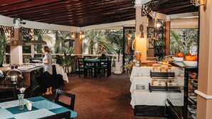 An indoor restaurant with a brick floor, tables with blue and white tablecloths, and a buffet area with food displays.