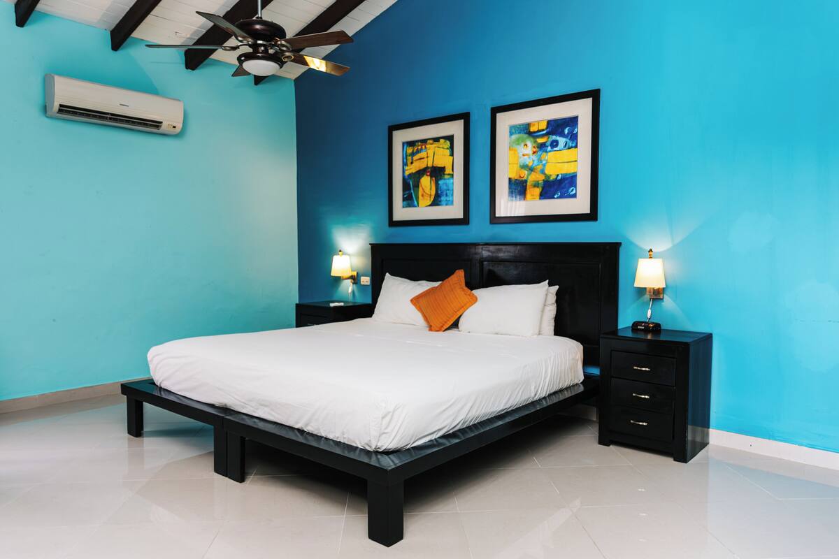 A bedroom with a bed, nightstands, a ceiling fan, and two framed artworks on the wall.
